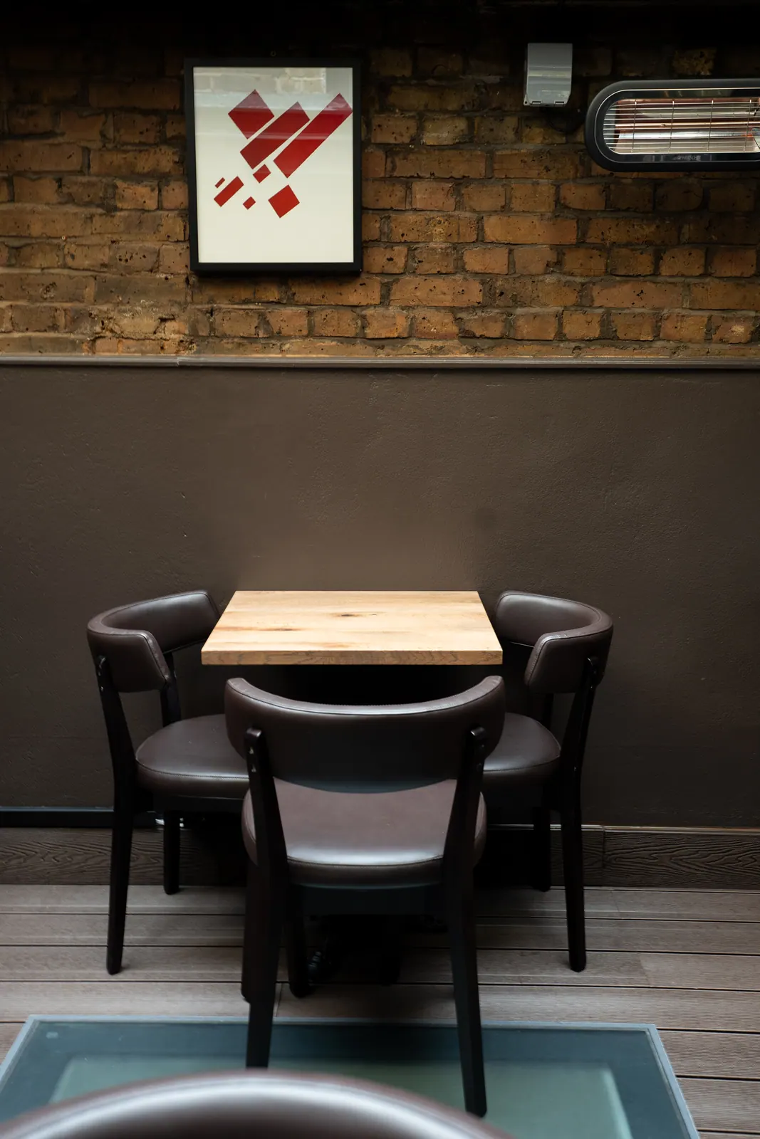 Square wood table and dark chairs against brick at Laika